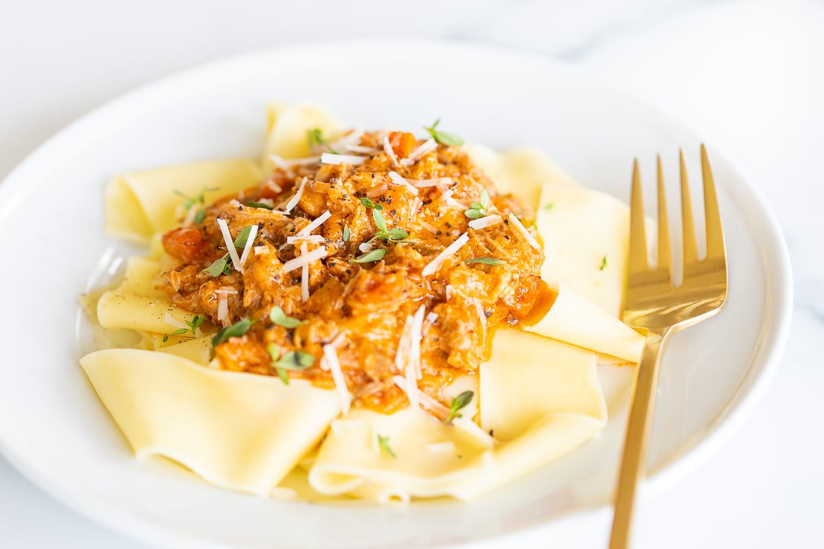 A white plate with a serving of braised pork ragu with pappardelle