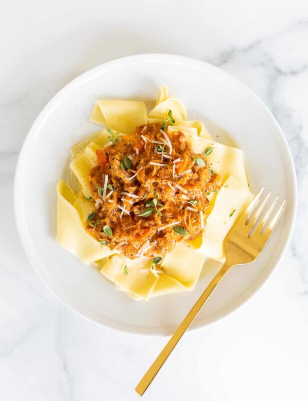 A white plate filled with pork ragu over pappardelle.