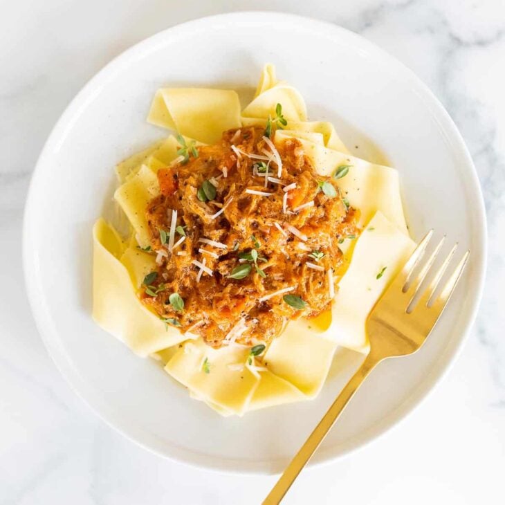 A white plate filled with pork ragu over pappardelle.