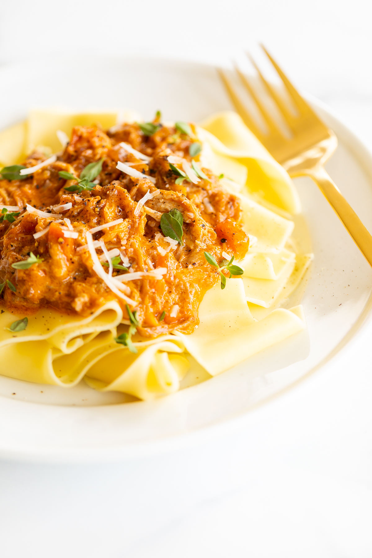 A white plate with a serving of braised pork ragu with pappardelle