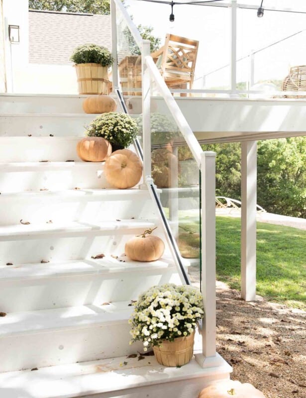 White deck steps decorated with minimalist fall decor, peach pumpkins and white mums.