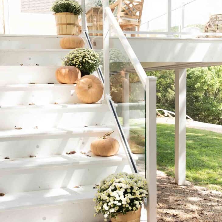 White deck steps decorated with minimalist fall decor, peach pumpkins and white mums.