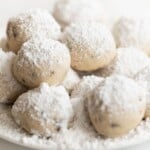 A plate of chocolate chip pecan snowball cookies, dusted in powdered sugar.