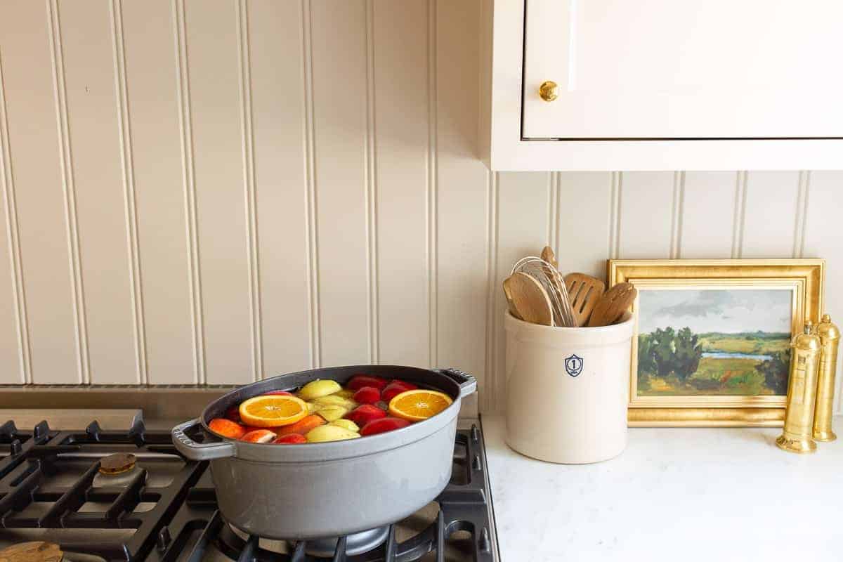 Two cast iron pots on a stove in a white kitchen filled with a homemade apple cider recipe simmering.
