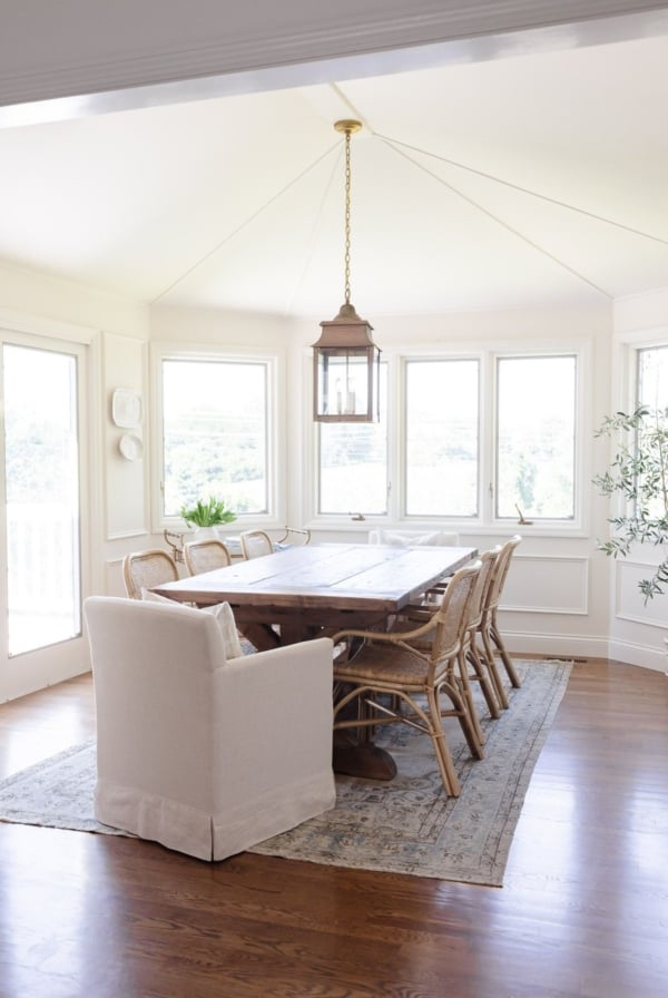 A white dining room with a rustic wood table and a vintage Turkish rug on the floor.