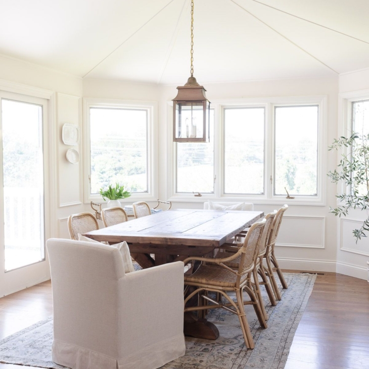A white dining room with a rustic wood table and a vintage Turkish rug on the floor.
