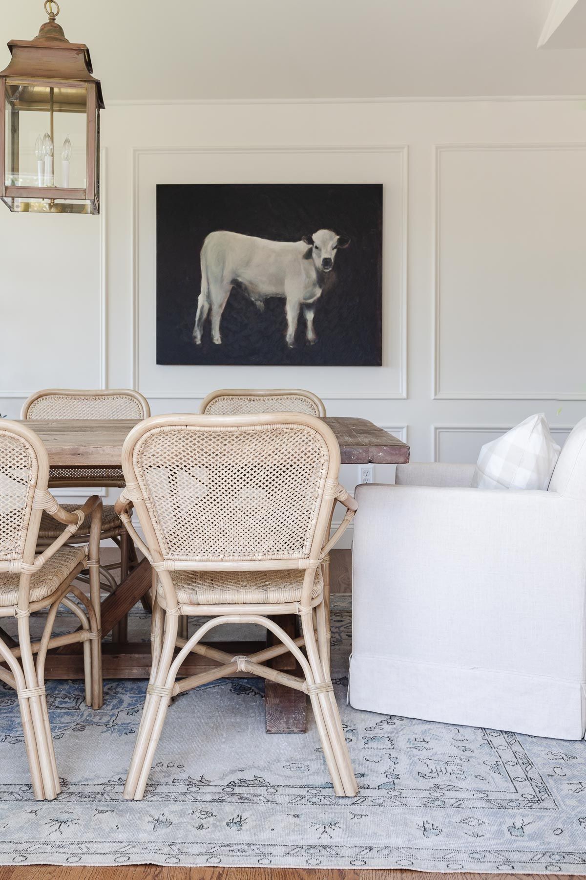 A white dining room with a rustic wood table and a vintage Turkish rug on the floor.