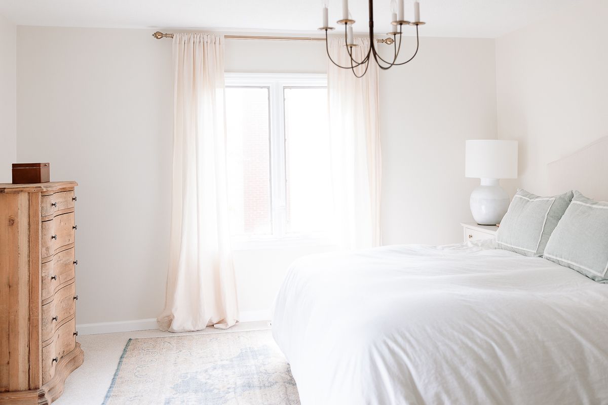 A white bedroom with a soft blue vintage Turkish rug on the floor, over carpet.