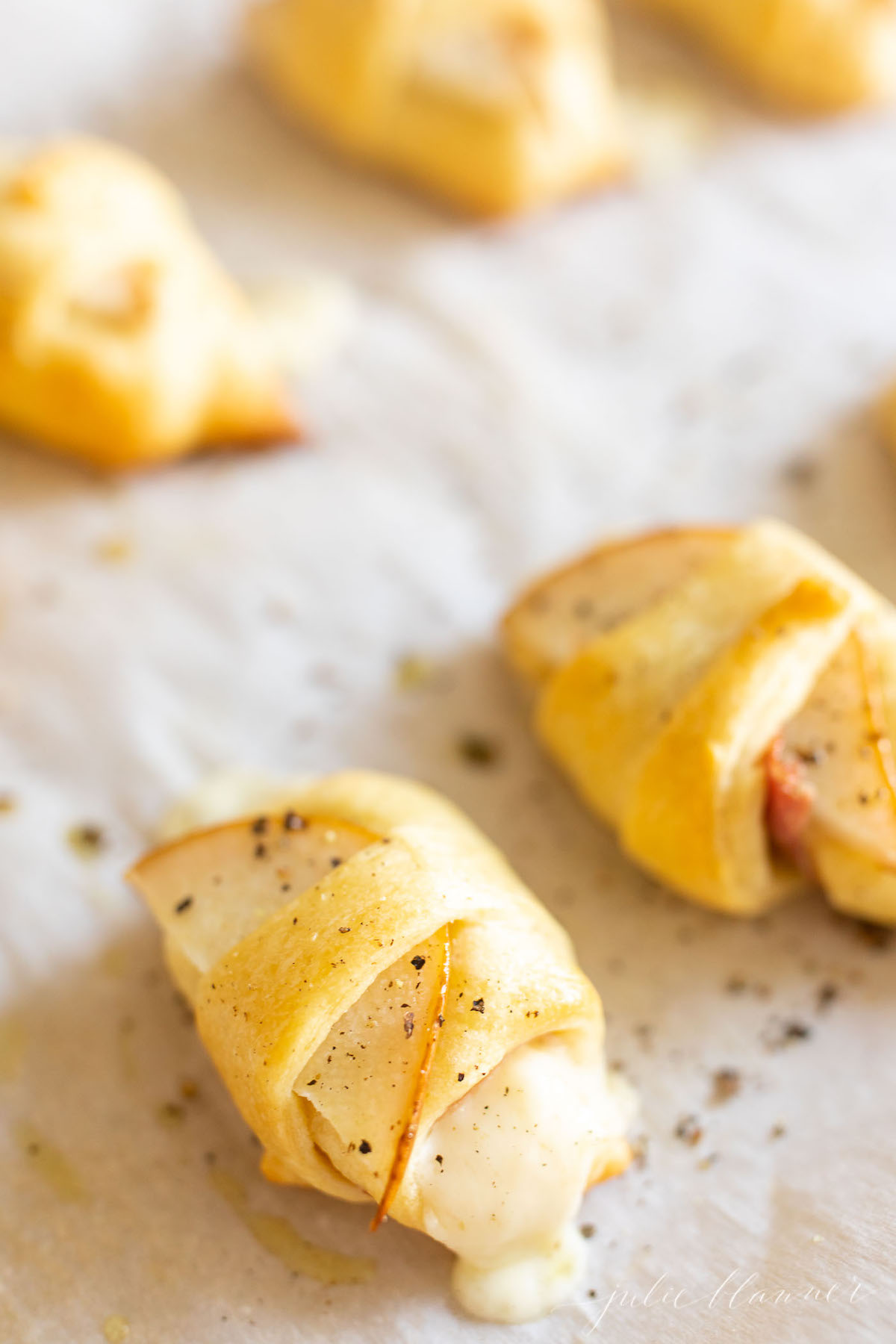 Pear wrapped crescent roll appetizers on a parchment lined baking sheet.