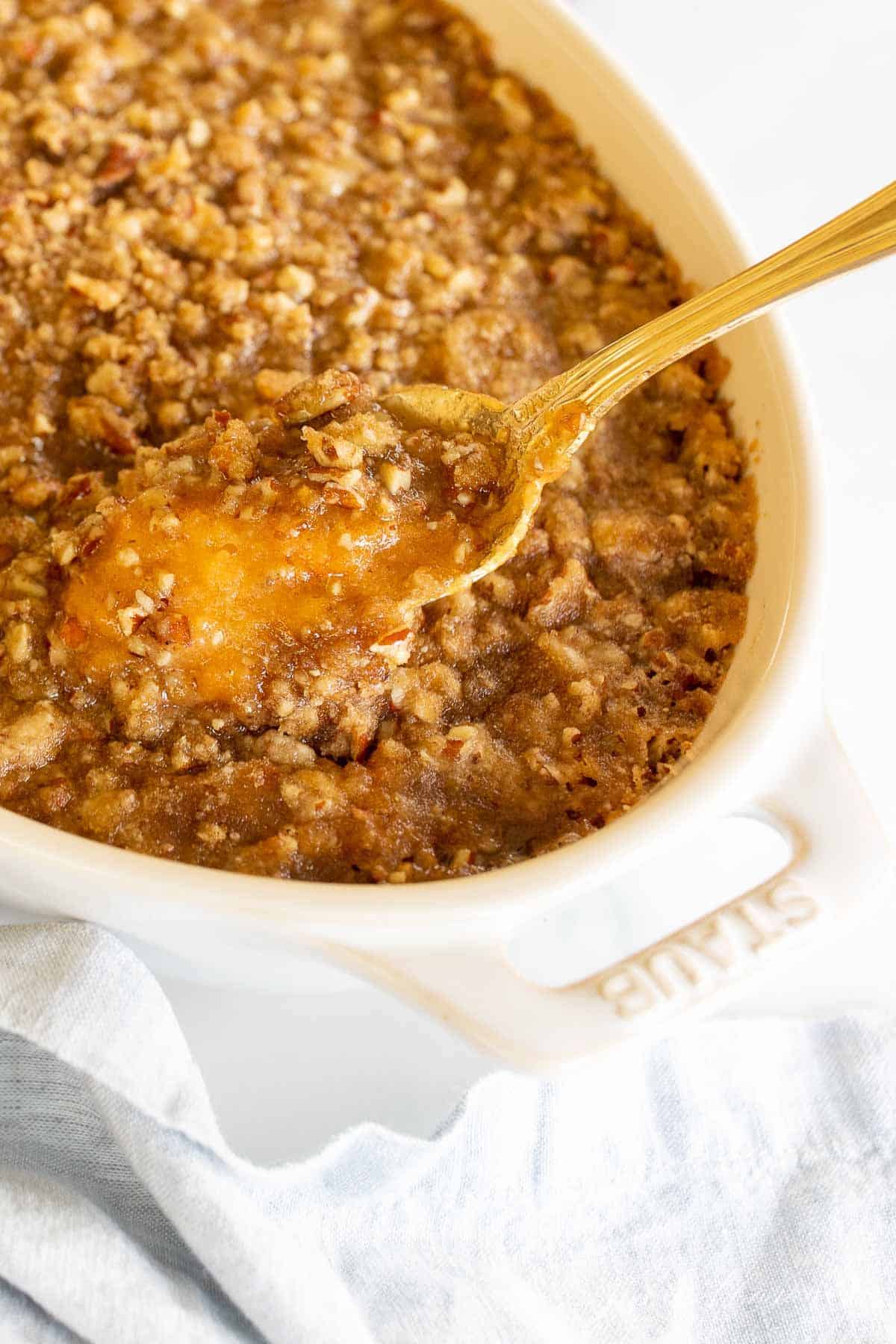 A white oval baking dish filled with a sweet potato casserole, spoon lifting out a serving.