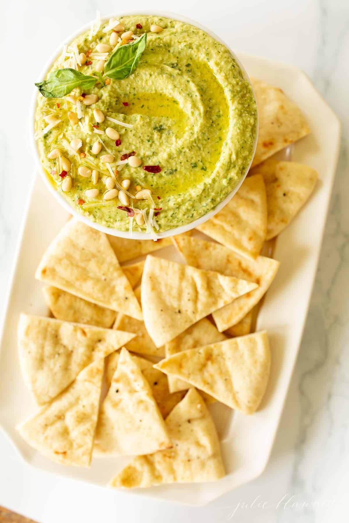 A platter full of pita triangles with a bowl full of basil hummus.