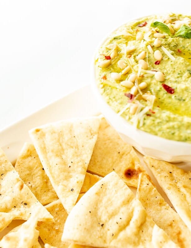 A platter full of pita triangles with a bowl full of basil pesto hummus.