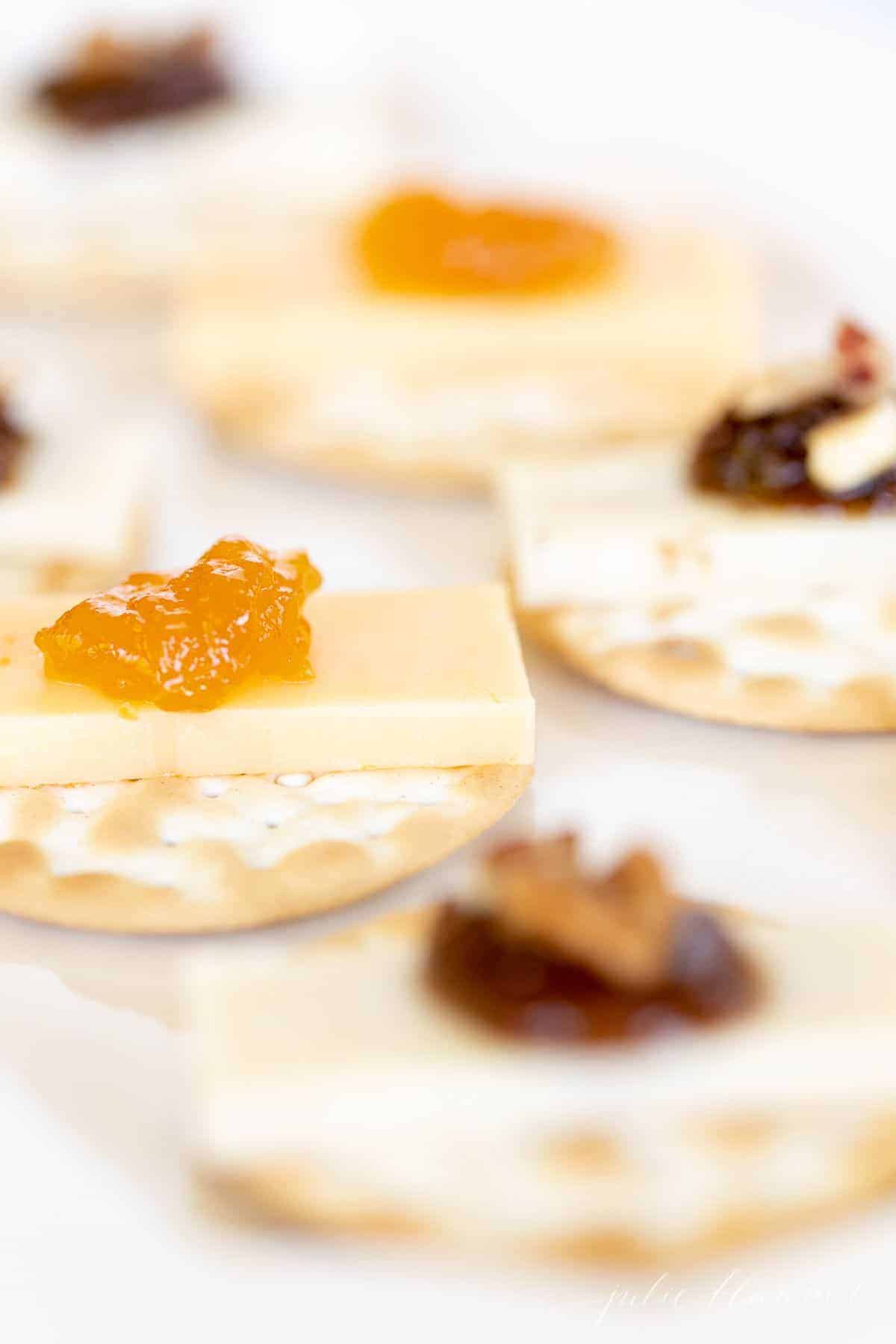A cheese and cracker display with cheese, jam and nuts.