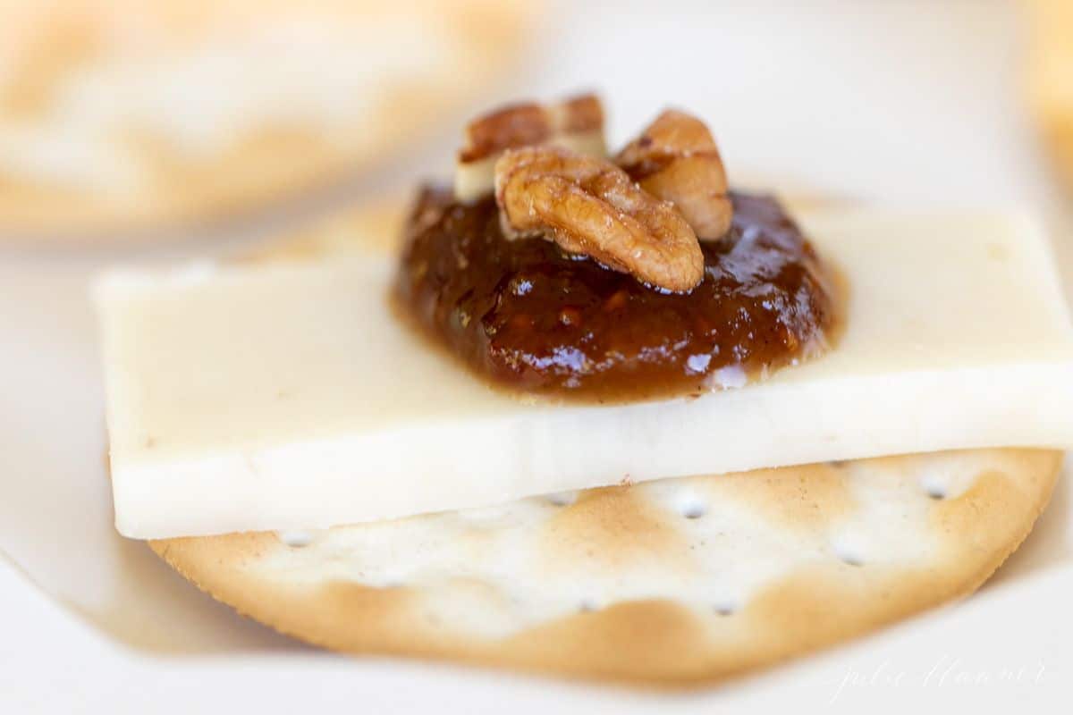 A cracker stacked with cheese, jam and nuts.