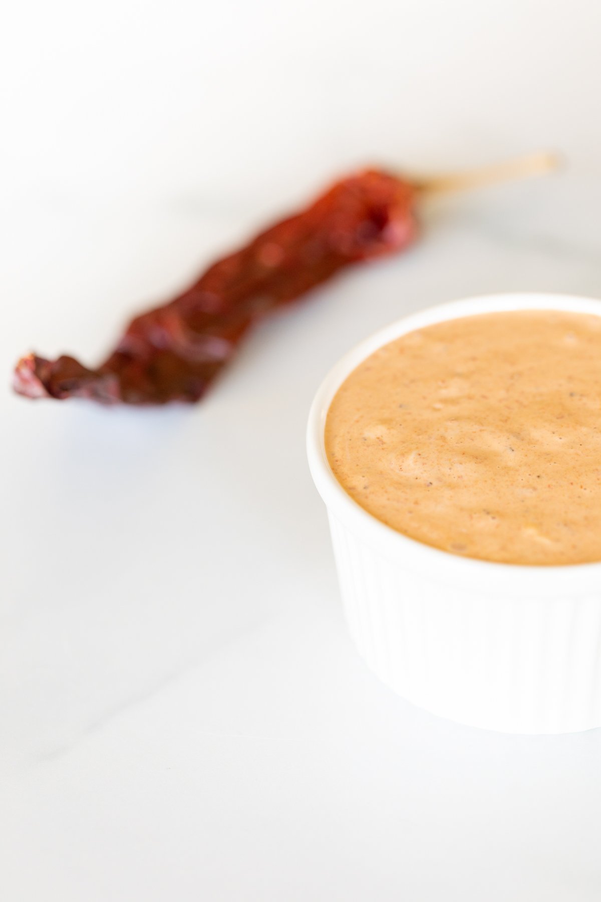 A white bowl of chipotle aioli with chipotle pepper in background.
