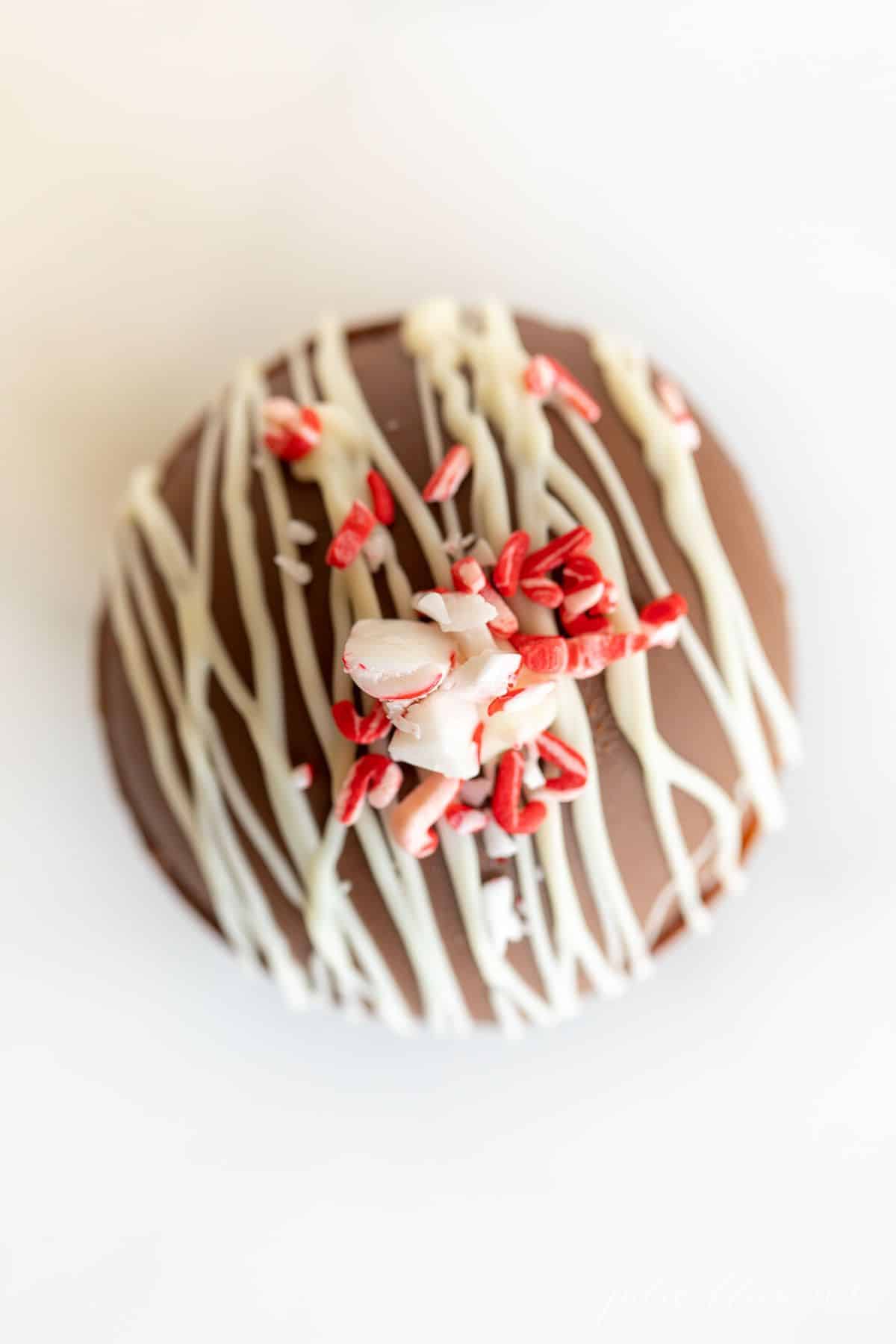 A single hot chocolate bomb on a marble surface, drizzled with white chocolate and topped with crushed peppermint.