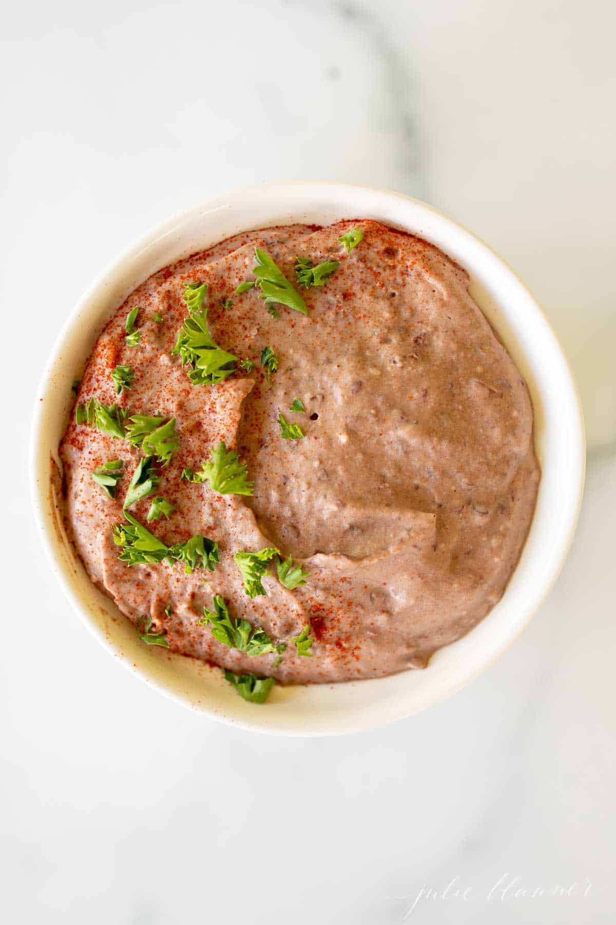 A white bowl full of black bean hummus topped with herbs