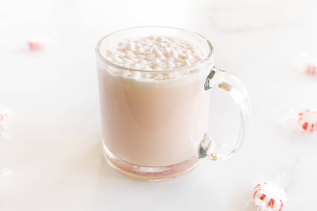 A clear glass mug of peppermint hot chocolate, topped with tiny marshmallows and crushed peppermint.