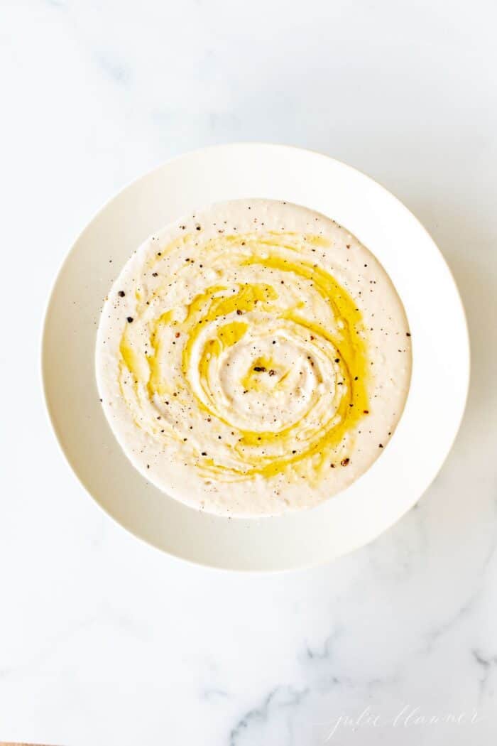 A white bowl filled with homemade white bean dip, drizzled with olive oil.