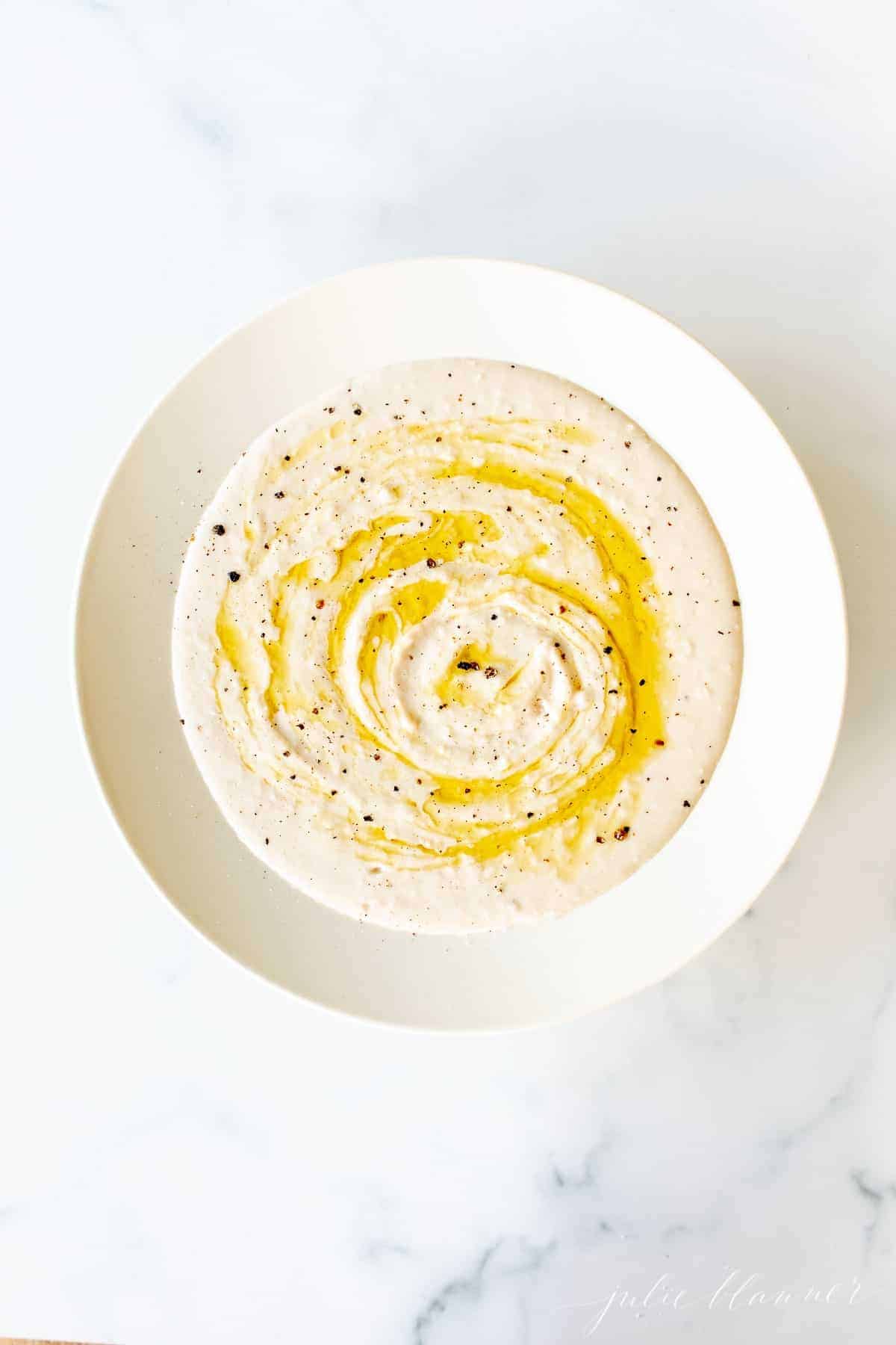 A white bowl filled with homemade white bean dip, drizzled with olive oil.
