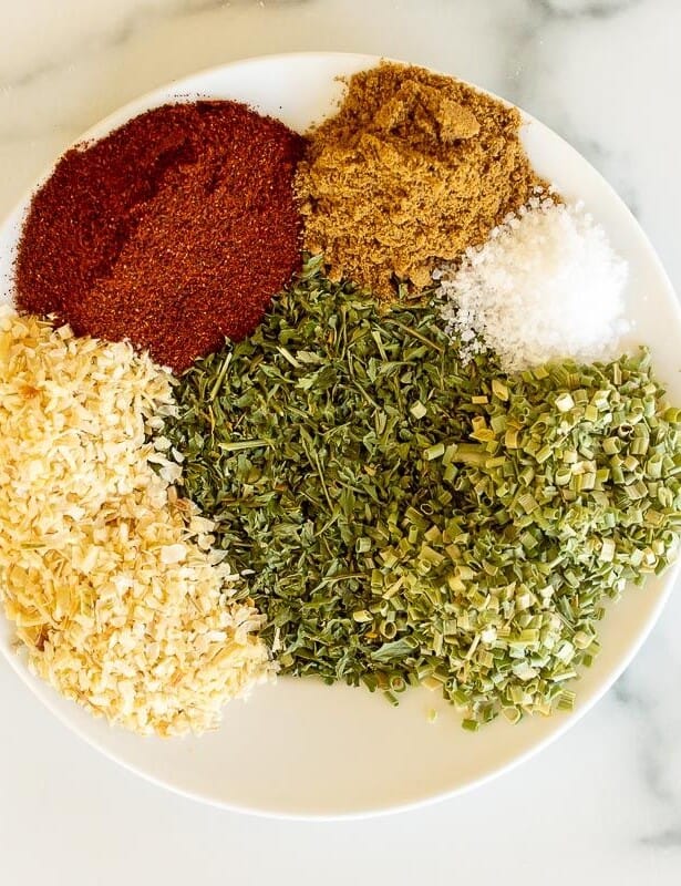 A white plate on a marble surface, topped with individual piles of spices for a homemade fiesta ranch mix.