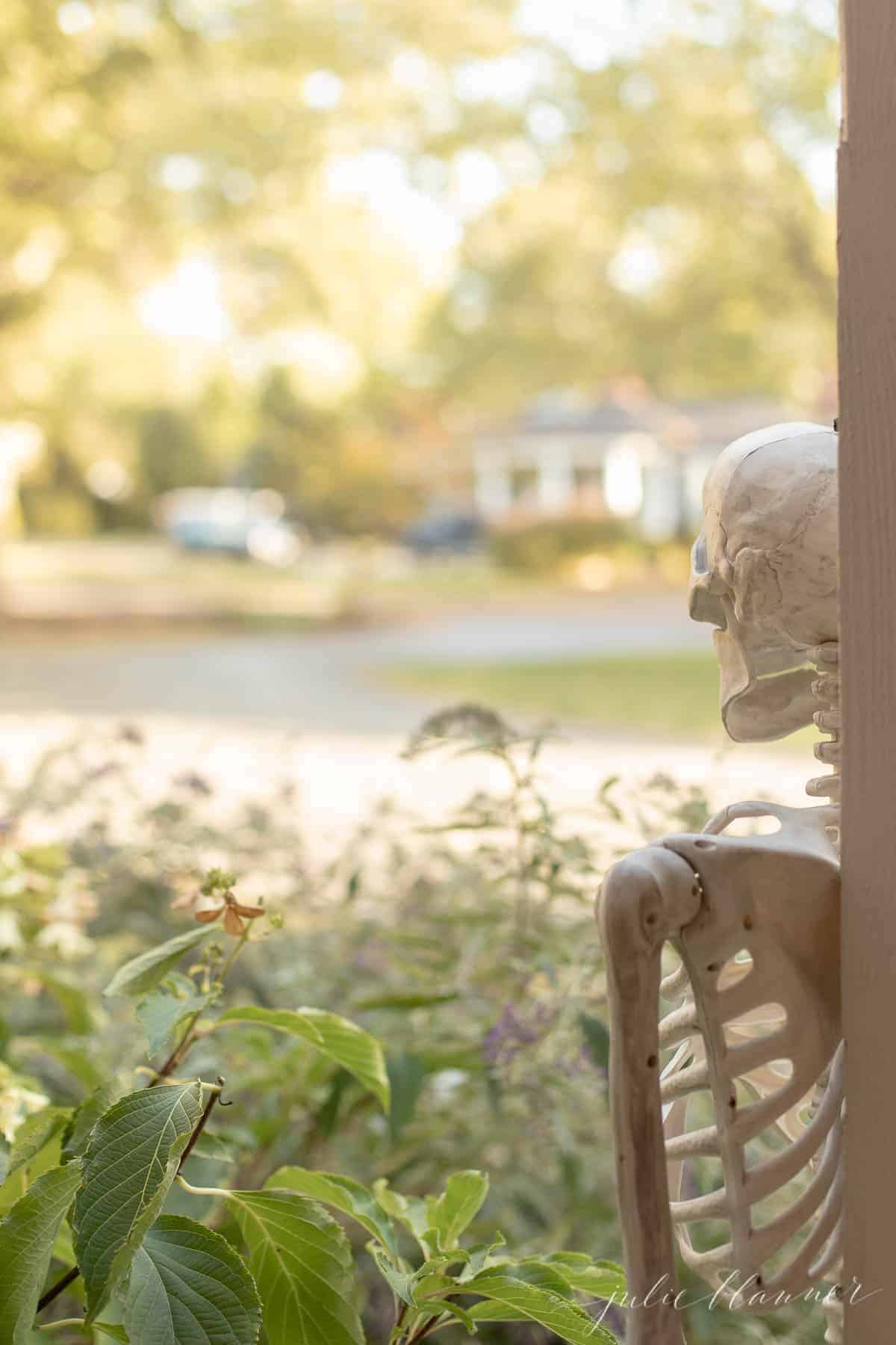 A life size skeleton leaning against a porch pillar for Halloween front porch decor.
