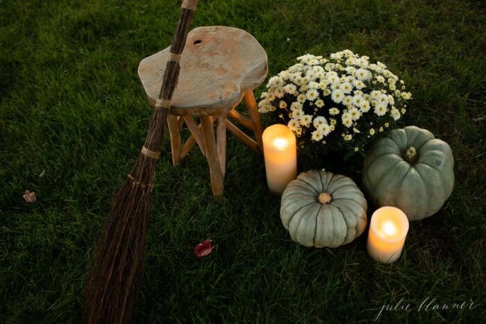 Mums, heirloom candles and a witch's broom set up for Halloween decorations on the grass.