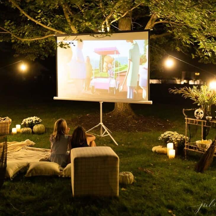 An outdoor movie set up in a yard for halloween, with a skeleton, candles and decorations.