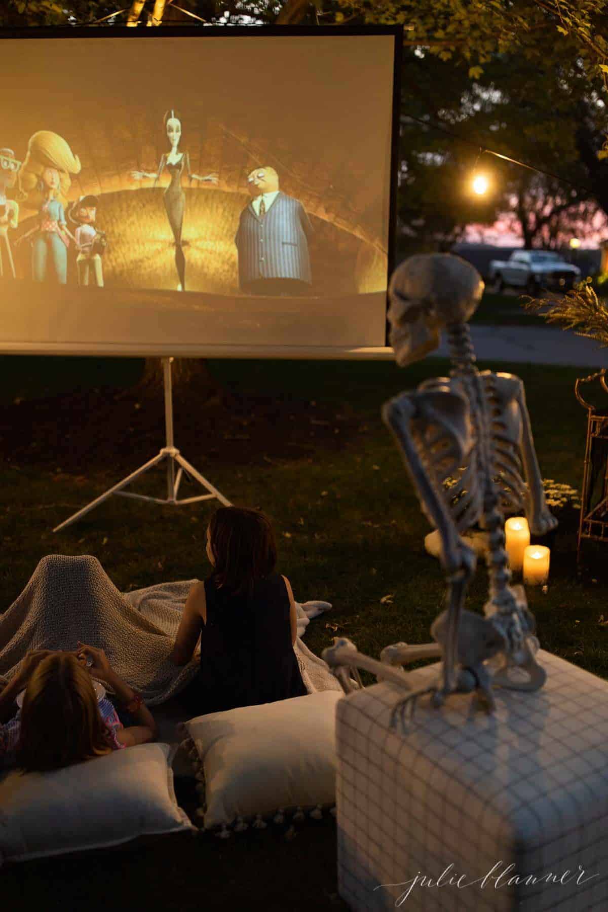 An outdoor movie set up in a yard for halloween, with a skeleton, candles and decorations.