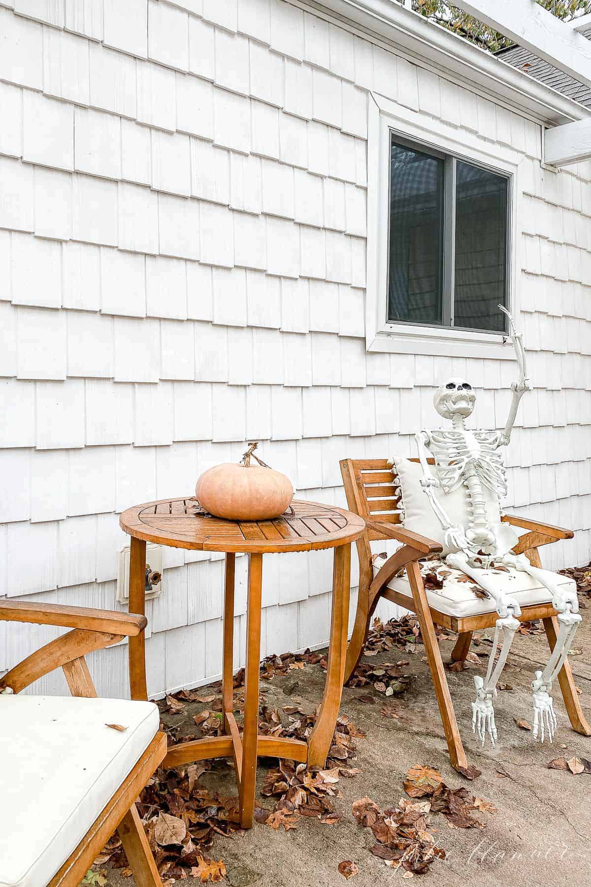 A wooden table set on a front porch with a skeleton waving for Halloween porch decorations.