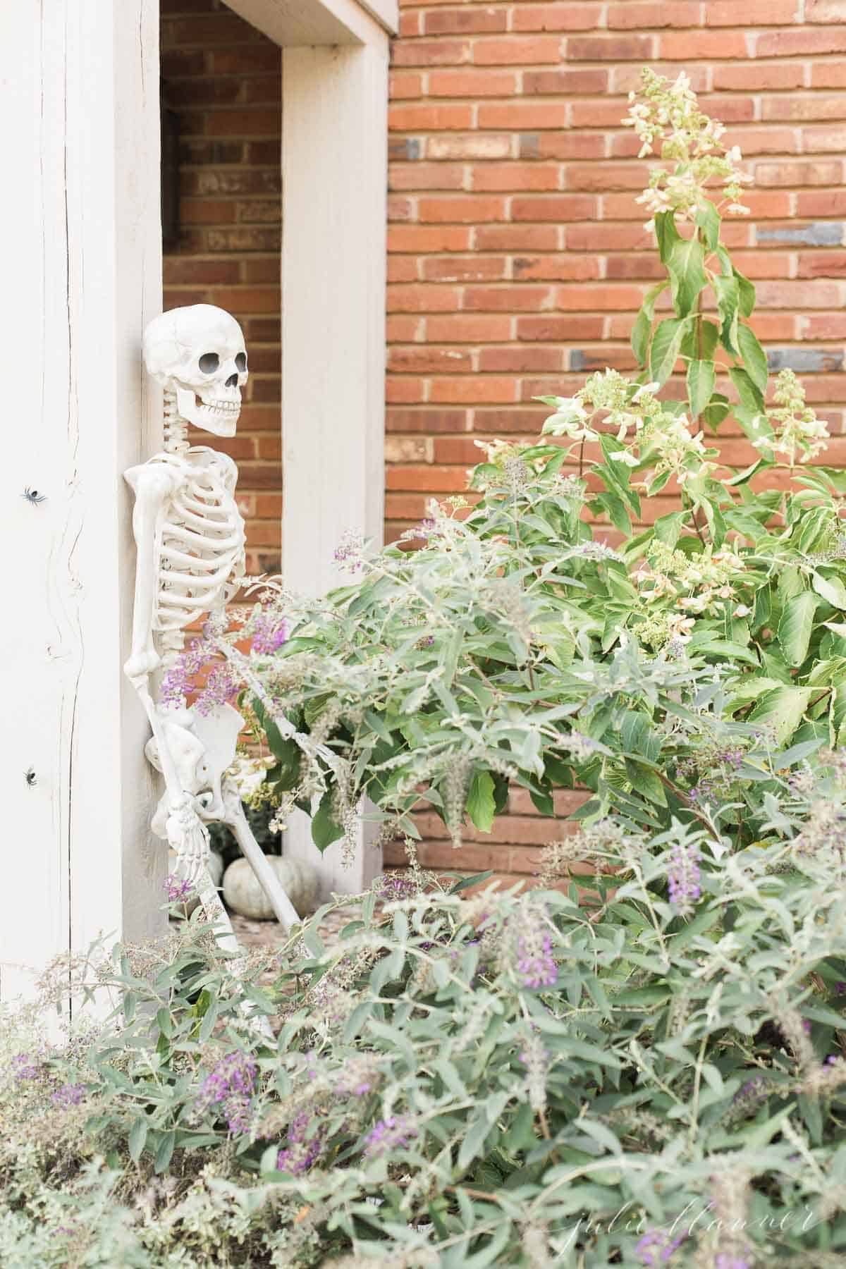 A life size skeleton leaning against a porch pillar for Halloween front porch decor.