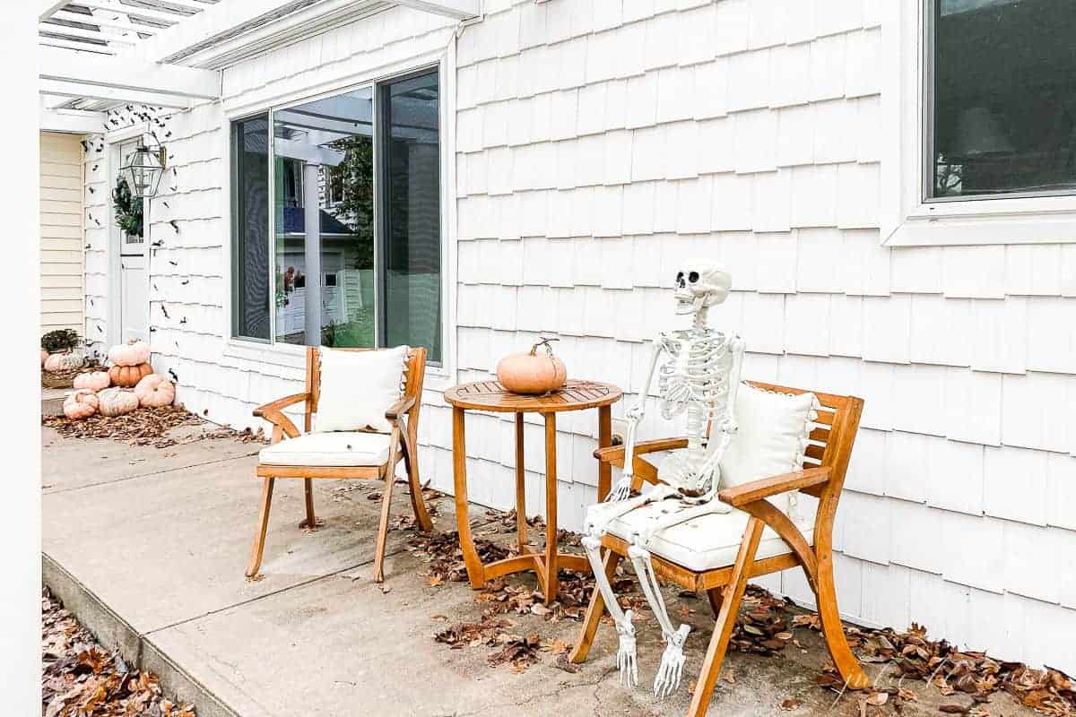 A wooden table set on a front porch with a skeleton waving for Halloween porch decorations.