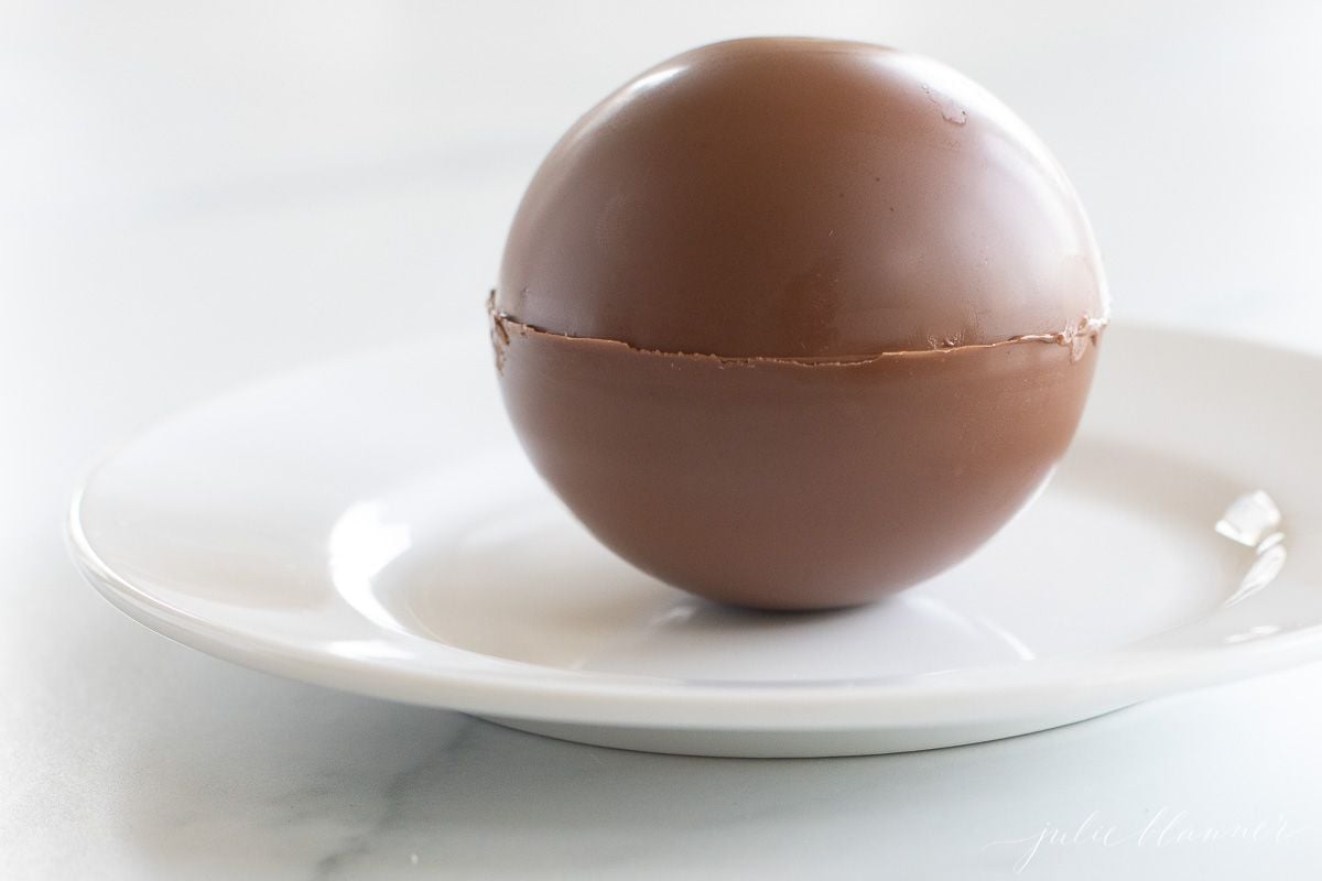 A white plate with a single hot chocolate bomb sphere.