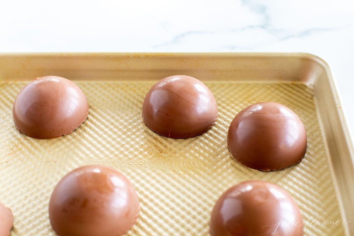 A gold baking sheet with half spheres of hot chocolate bombs.