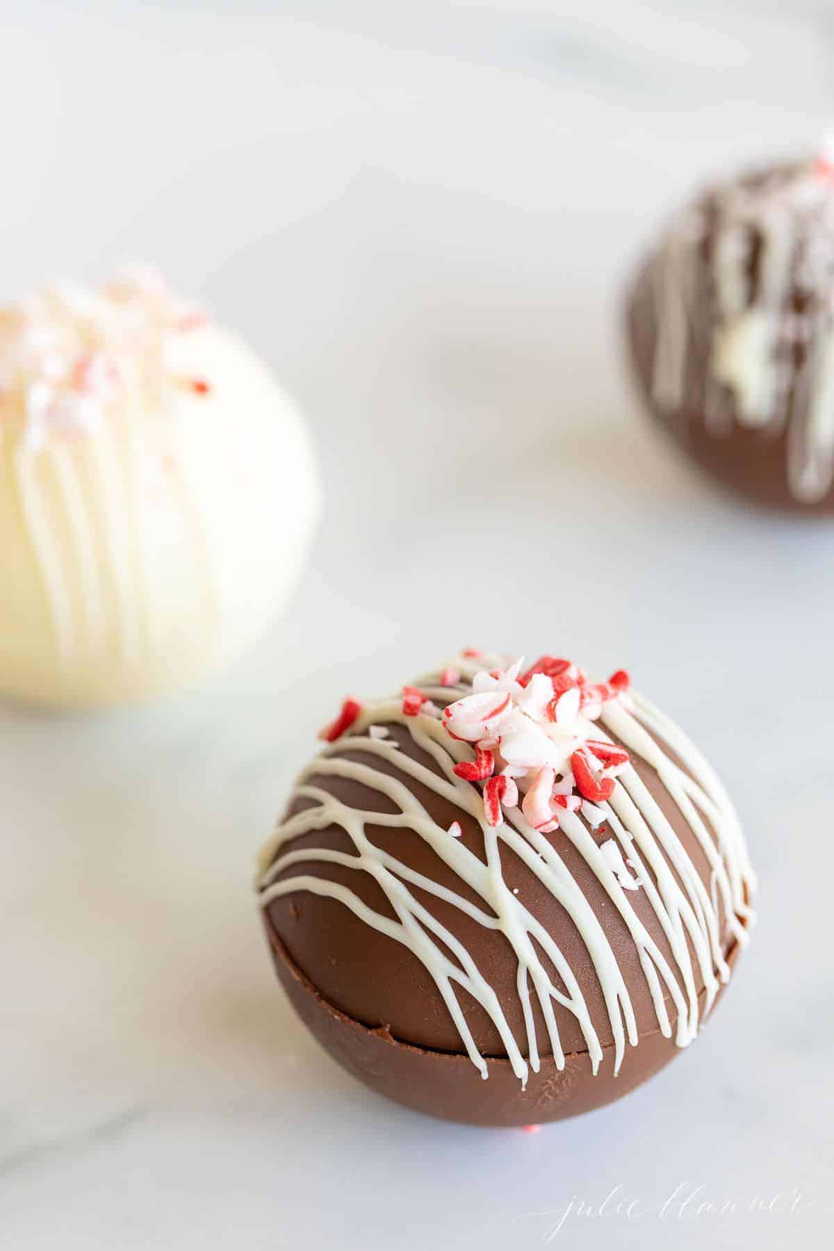 Three hot chocolate bombs on a marble surface, topped with crushed peppermint.