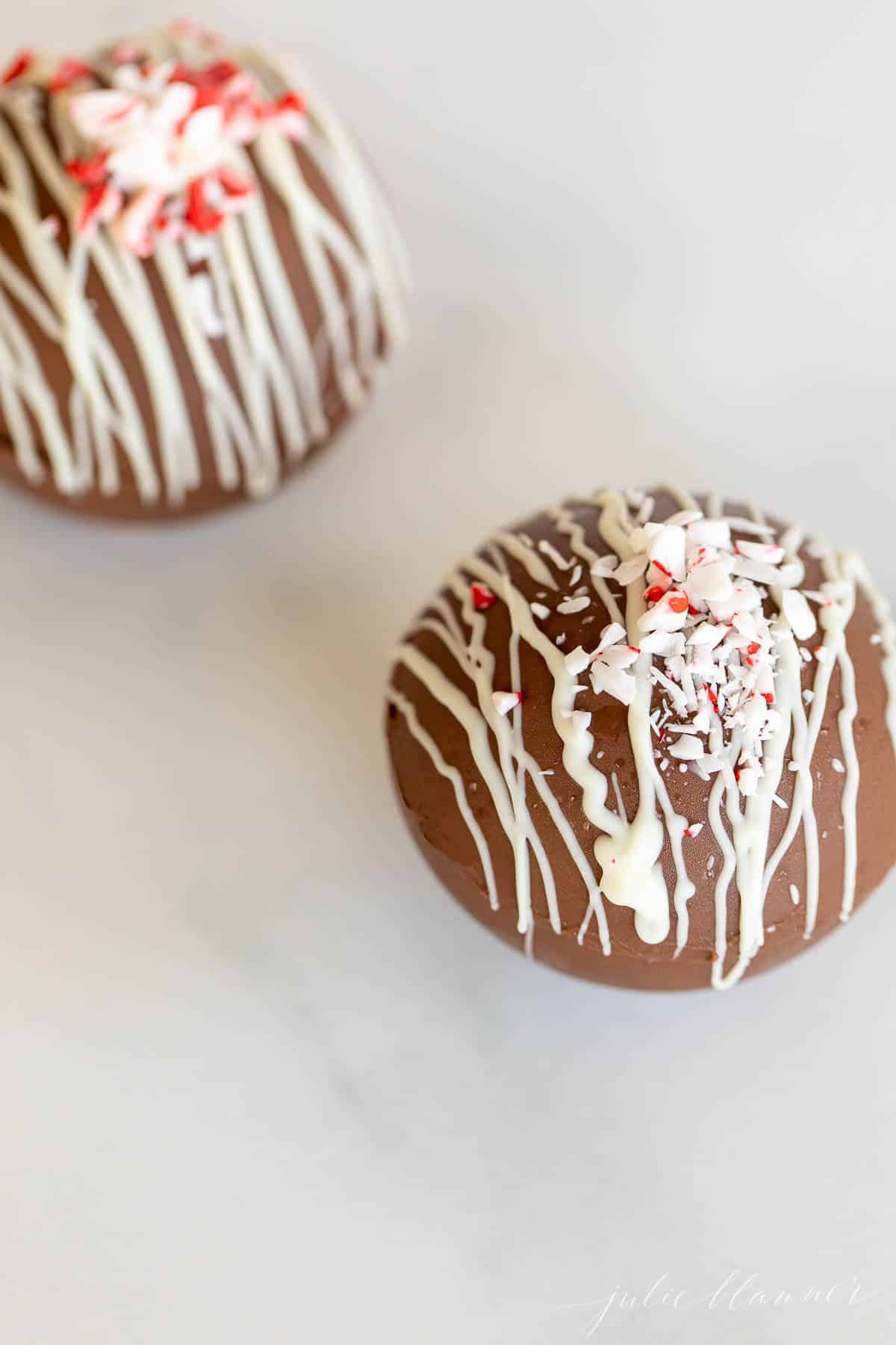 Two hot chocolate bombs on a marble surface, topped with crushed peppermint.