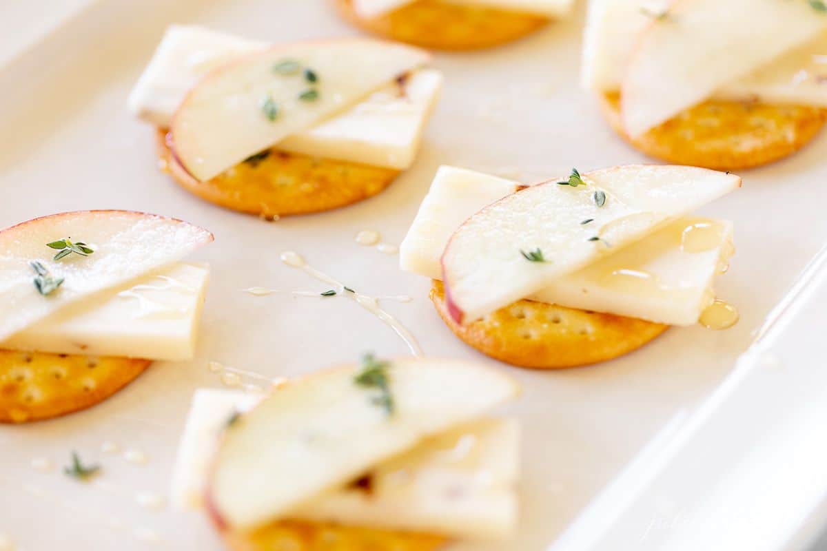 Cheese and cracker display with apples stacked on top of cheddar.