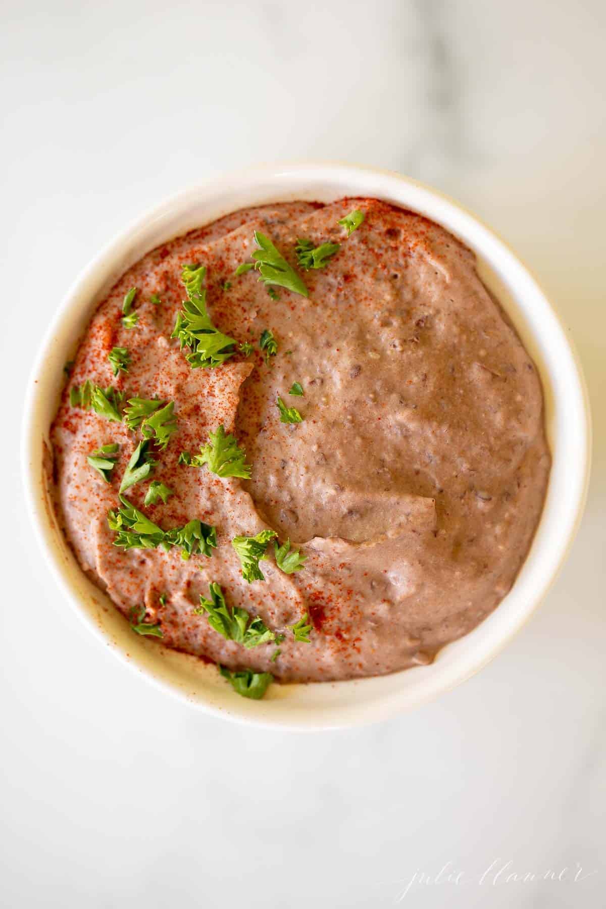 A white bowl full of black bean hummus topped with herbs