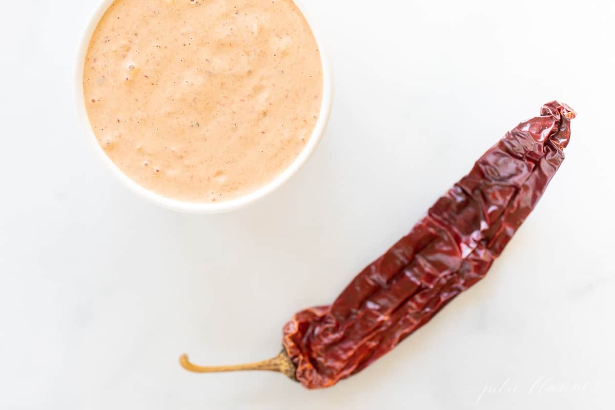 A white bowl of chipotle aioli with chipotle pepper in foreground.