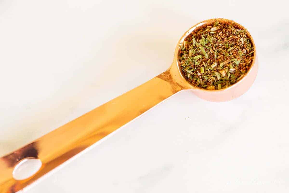 A copper measuring spoon on a white surface, filled with a homemade fiesta ranch seasoning mix.