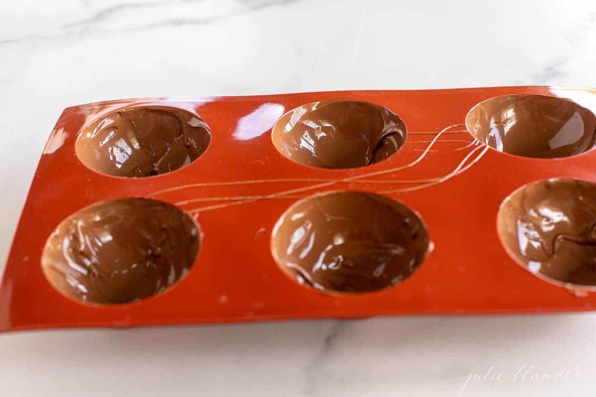 A red silicone sphere mold filled with melted chocolate.