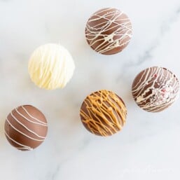 A marble surface with hot chocolate bombs in different colors and decorated styles.