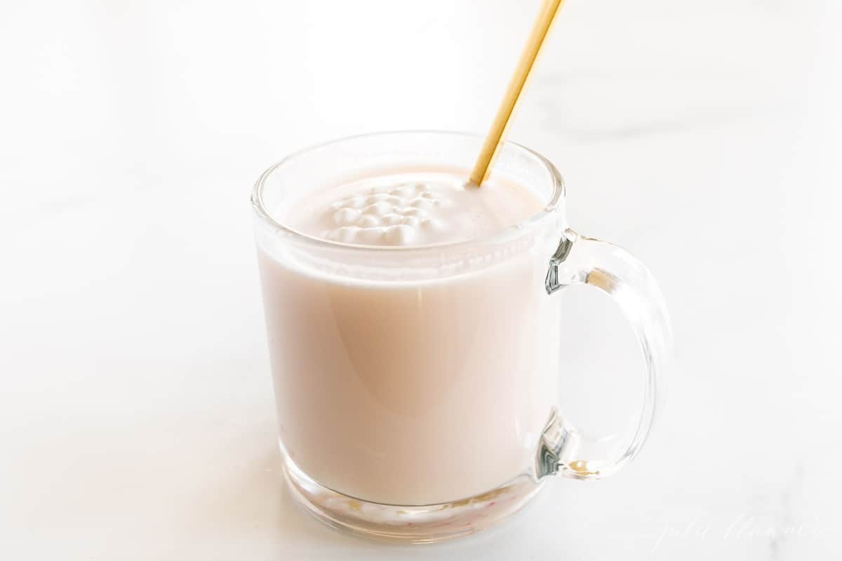 A clear glass mug of peppermint hot chocolate, gold spoon sticking out of mug.