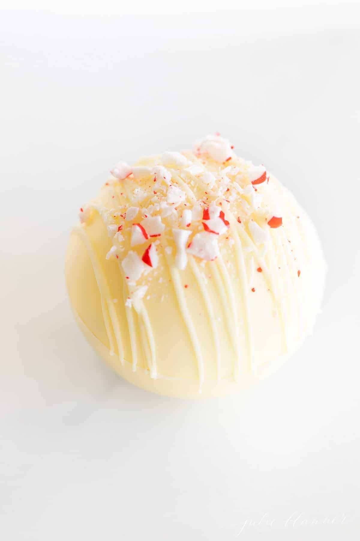 A white chocolate hot chocolate bomb topped with crushed peppermint on a marble surface.