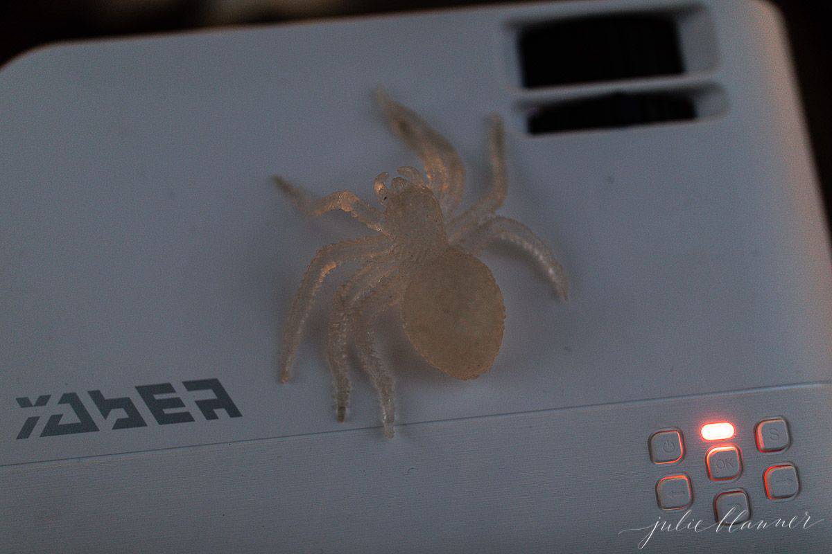 A projector for an outdoor movie night for Halloween, with a plastic spider on top.