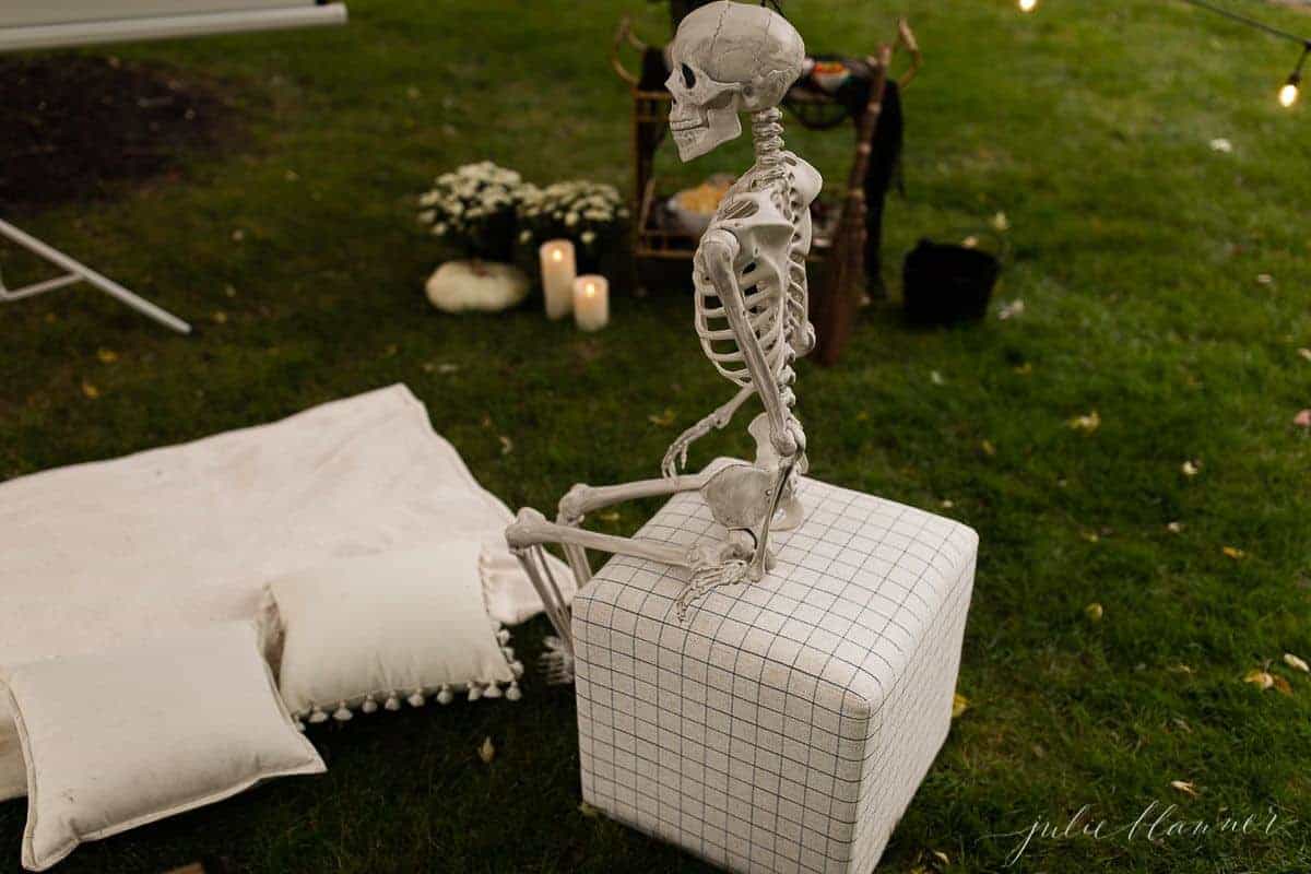 An outdoor movie set up in a yard for halloween, with a skeleton, candles and decorations.