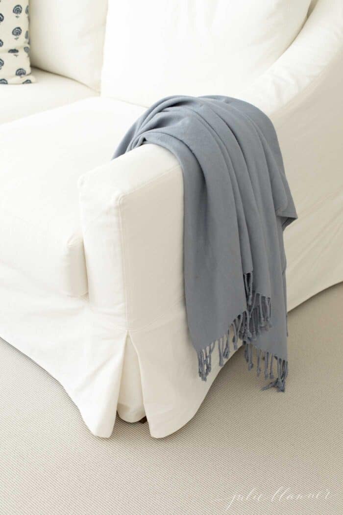 A cream colored indoor outdoor rug that looks like sisal, under a white sofa with a blue blanket draped over the arm.