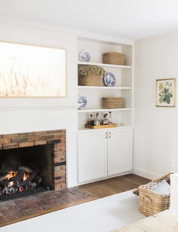 A white living room with a fireplace, built in bookshelves, and a living room rug over hardwood floors.
