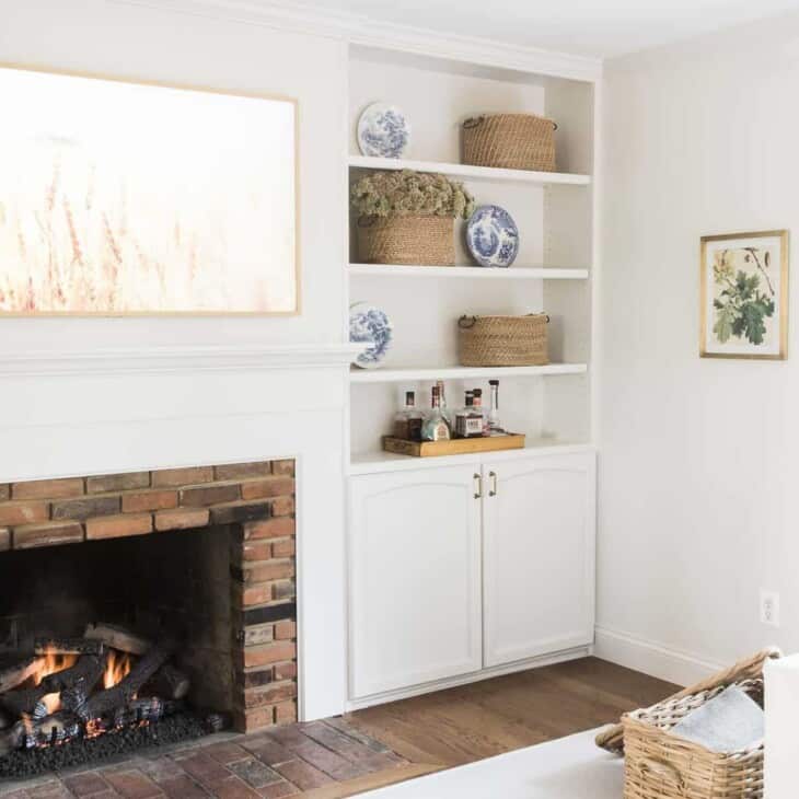 A white living room with a fireplace, built in bookshelves, and a living room rug over hardwood floors.