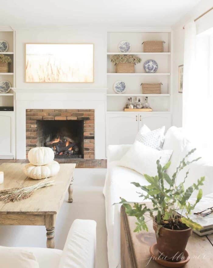 A white living room with a fireplace, built in bookshelves, and a coffee table decorated for fall.